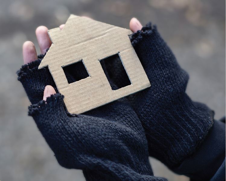 Brown cardboard house shape being held by two hands with black gloves