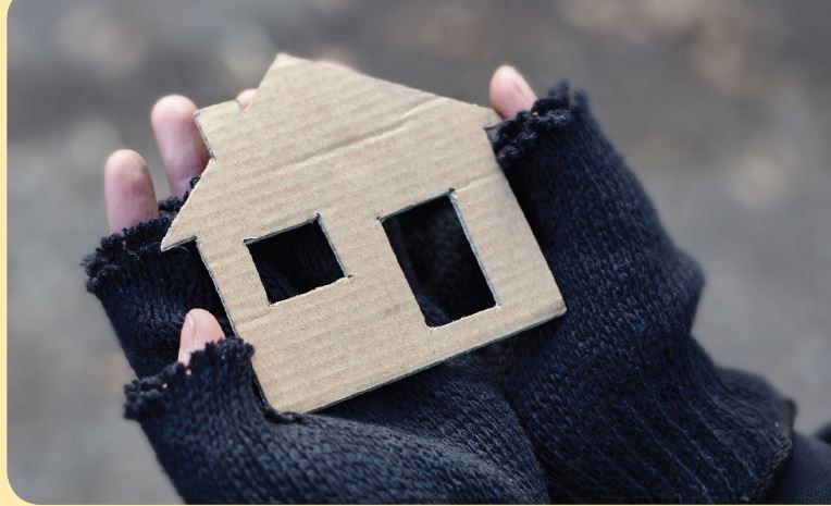 two hands cover in black gloves holding a cardboard house