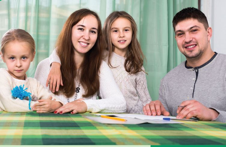 mother and father with two girls in he table helping with homework