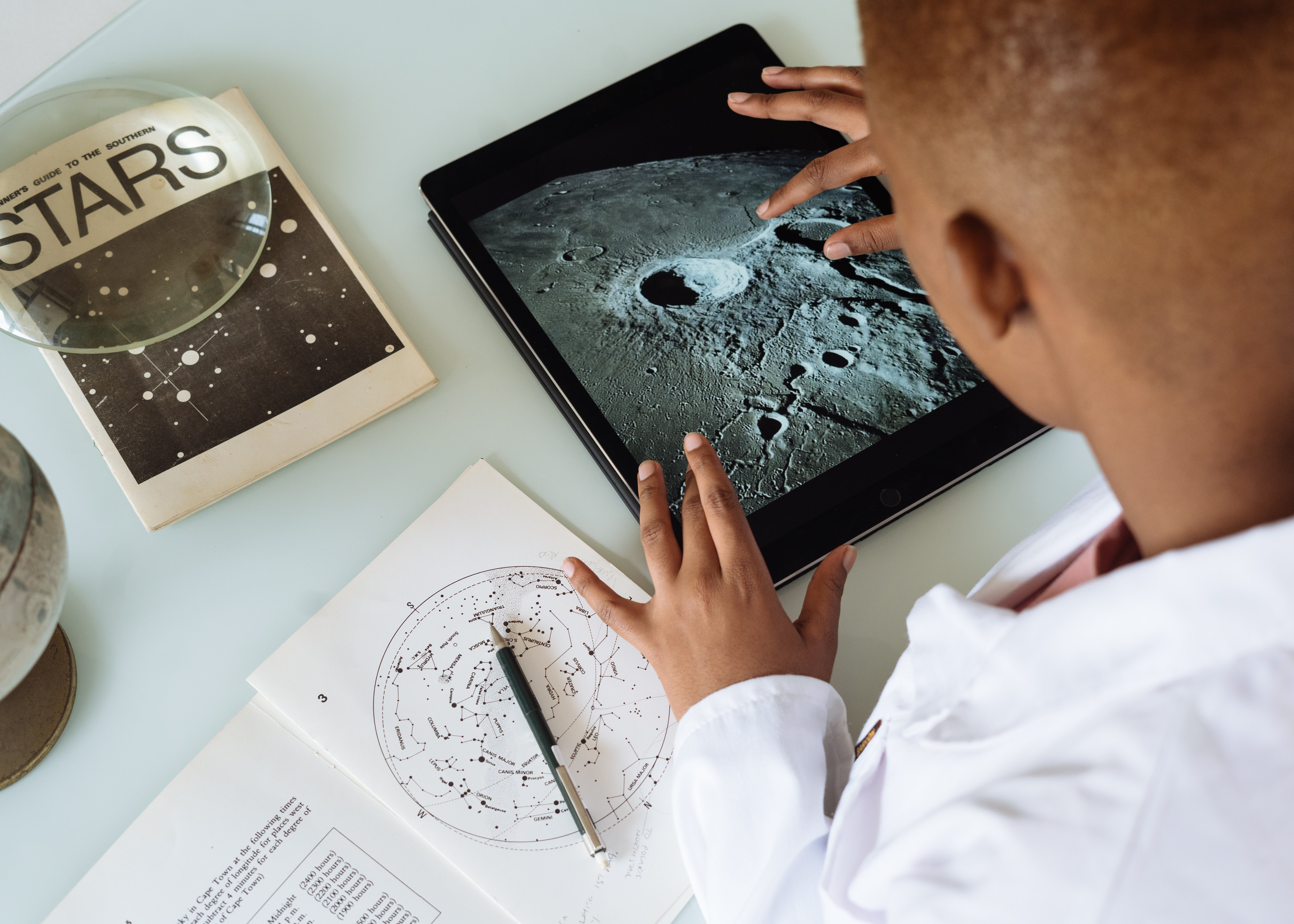 African American boy with star charts and tablet showing the moon.