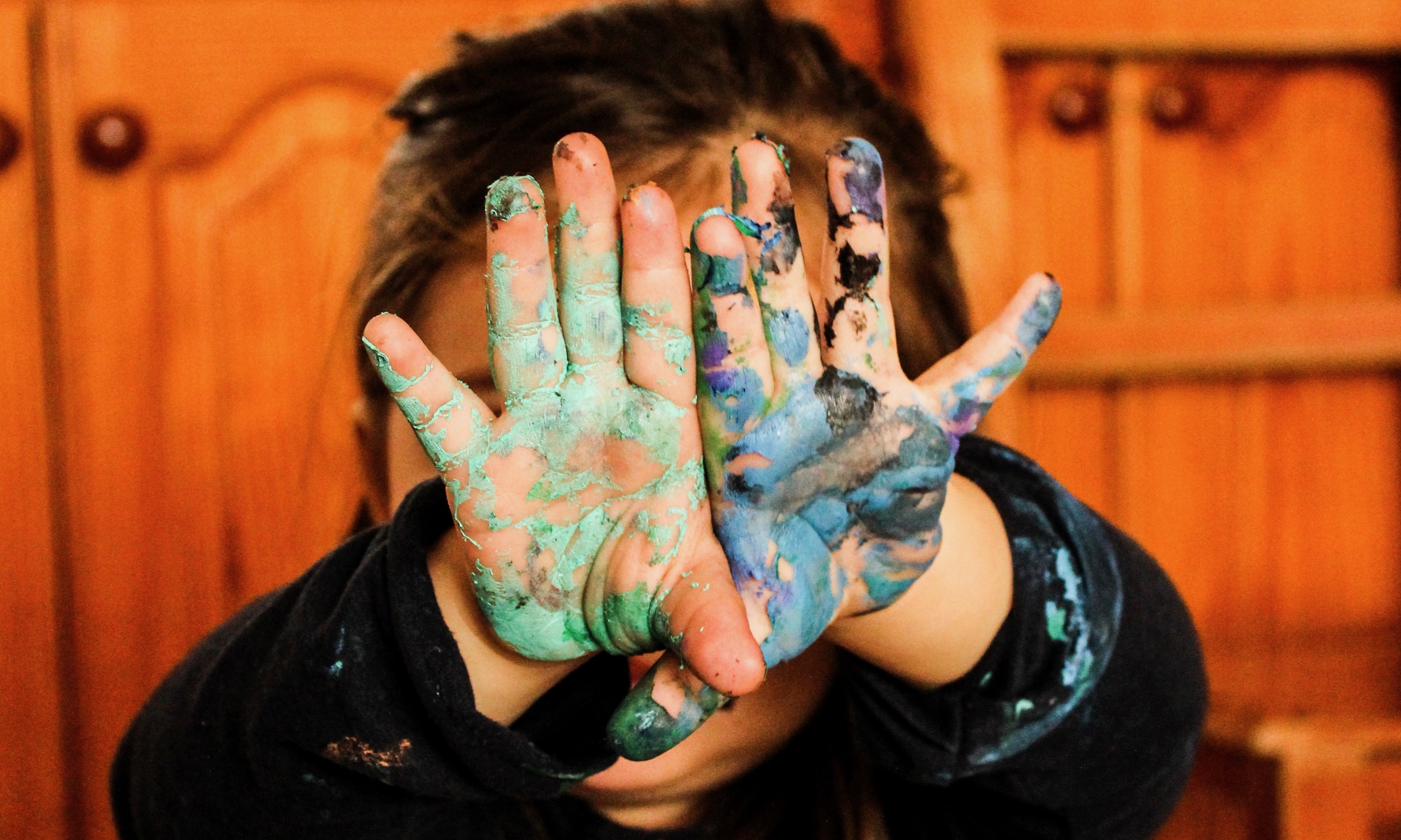 Child with painted hands in front of their face.